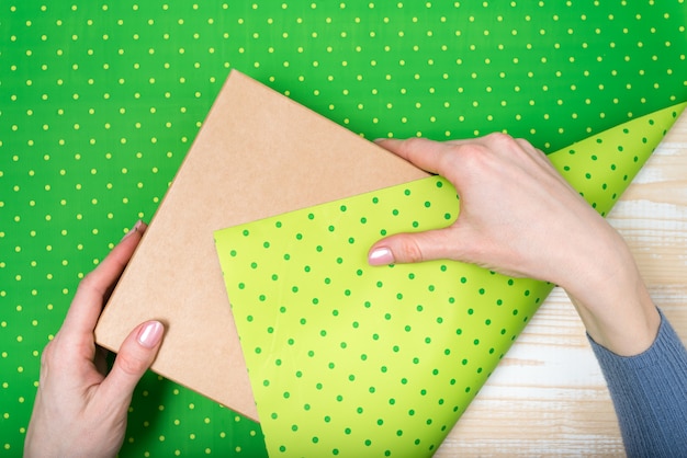 Vrouwelijke handen pakken een geschenk in een groene polka-dot papier, bovenaanzicht