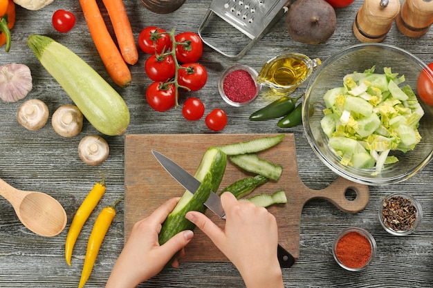 Vrouwelijke handen peeling komkommer bij tafelblad bekijken
