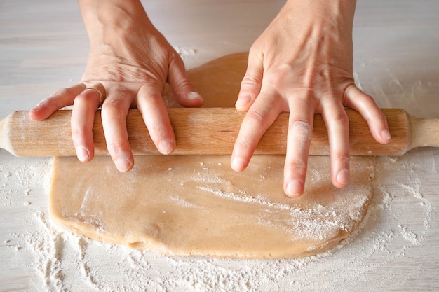 Vrouwelijke handen rollen deeg uit met een houten deegroller