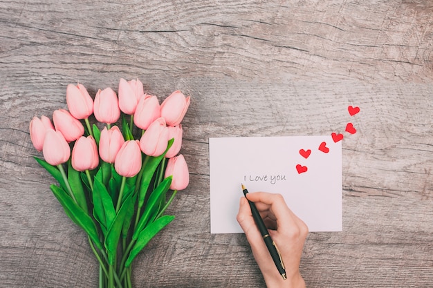 Vrouwelijke handen schrijven een bericht van liefde op een witte envelop, op een houten achtergrond. Valentijnsdag