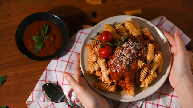 Vrouwelijke handen serveren een bord Italiaanse fusilli pasta met tomatensaus op een houten eettafel