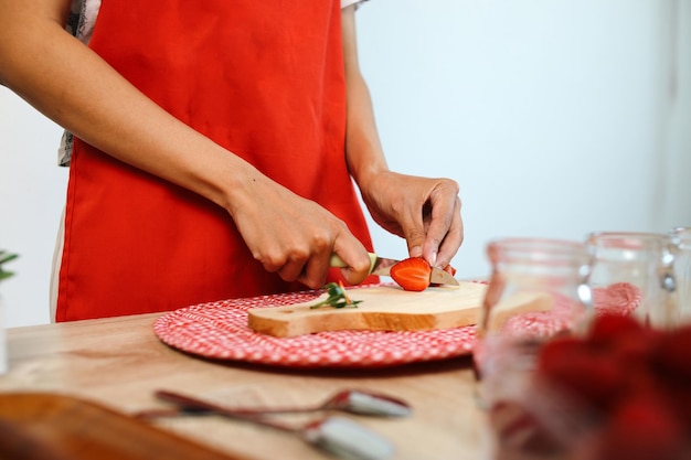 Vrouwelijke handen snijden aardbeien met een mes op een snijplank in de keuken