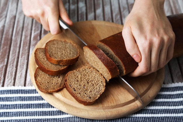 Vrouwelijke handen snijden brood op houten plank close-up