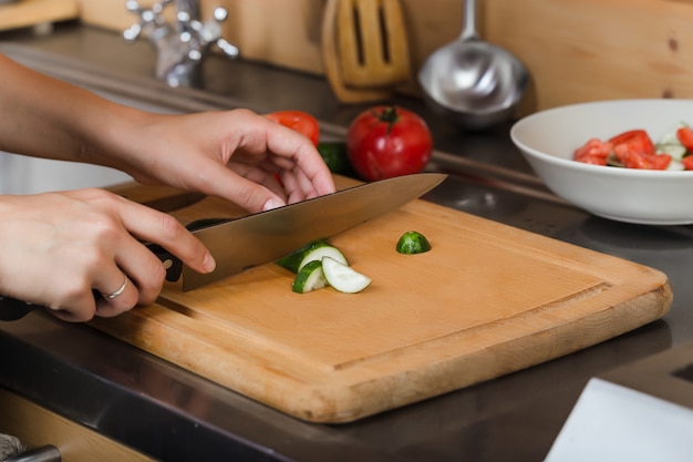 Vrouwelijke handen snijden een komkommer op het bord
