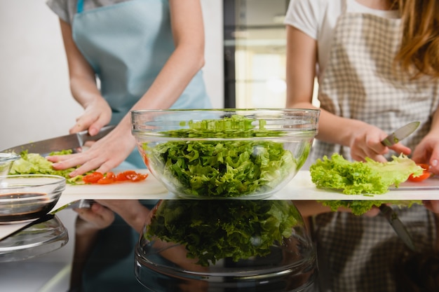 Vrouwelijke handen snijden groene salade in kom