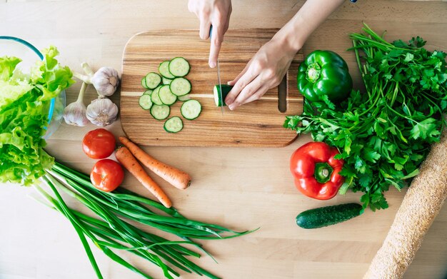 Vrouwelijke handen snijden groenten in de keuken. Vrouw die gezond voedsel kookt. Verse groenten op de snijplank. Concept van koken. Eetpatroon. Gezonde en veganistische levensstijl. Thuis koken. Eten koken