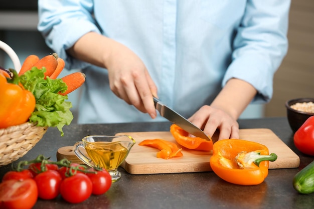 Vrouwelijke handen snijden peper aan tafel in de keuken