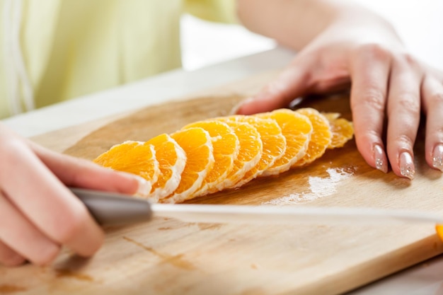 Vrouwelijke handen snijden sinaasappel in een keuken. Detailopname. Selectieve aandacht.