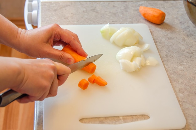 Vrouwelijke handen snijden wortelen en uien met mes op witte snijplank Voedsel bereiden Koken