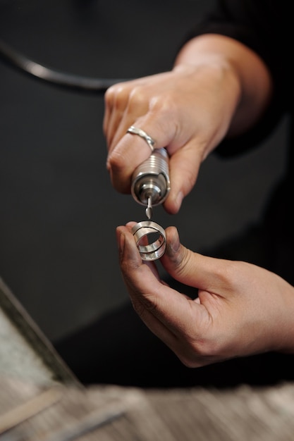 Vrouwelijke handen van bankjuwelier die zilveren ring vormen met behulp van polijstmachine in werkplaats