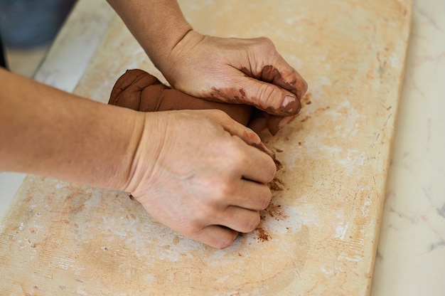 Vrouwelijke handen van de meester kneden rode klei. Voorbereiding op het werk in de pottenbakkerswerkplaats.