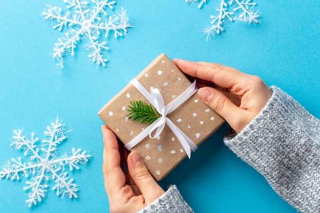 Vrouwelijke handen vanuit hoek met kerstcadeau in papieren verpakking op blauw met grote sneeuwvlokken