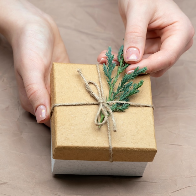 Vrouwelijke handen versieren bruine geschenkdoos met dennen takje