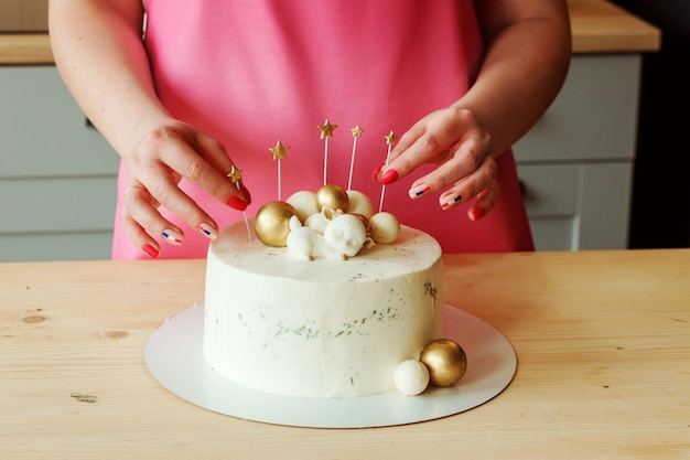 Vrouwelijke handen versieren heerlijke verjaardagstaart met sterren en ballen, roze schort op de achtergrond.