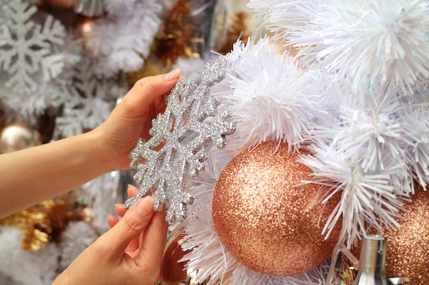 Vrouwelijke handen versieren kerstboom met een glitter sneeuwvlok gevormd ornament