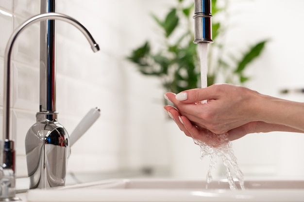 Vrouwelijke handen wassen in de gootsteen in de keuken of badkamer thuis, netheid, hygiëne en gezondheidsconcept