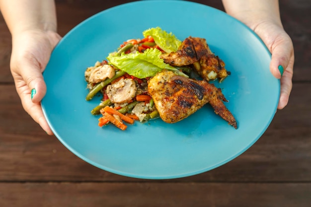 Vrouwelijke handen zetten een bord met gegrilde kip en groenten op tafel op straat