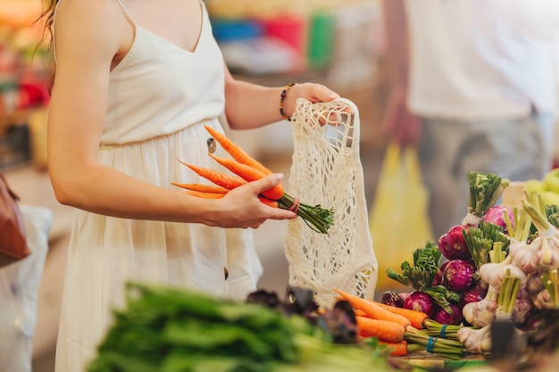 Vrouwelijke handen zetten groenten en fruit in een katoenen zak op de voedselmarkt. Herbruikbare eco-tas om te winkelen. Geen afvalconcept.