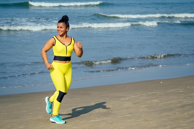Vrouwelijke hardloper joggen tijdens buitentraining op het strand Mooi fit gemengd ras Fitness model buitenshuis in geel zwart stijlvol yogapak