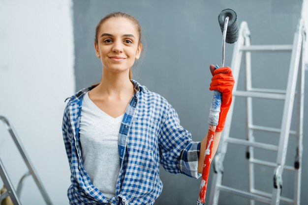 Vrouwelijke huisschilder met verfroller zittend op een ladder. Huisreparatie, gelukkige vrouw die appartementsrenovatie doet