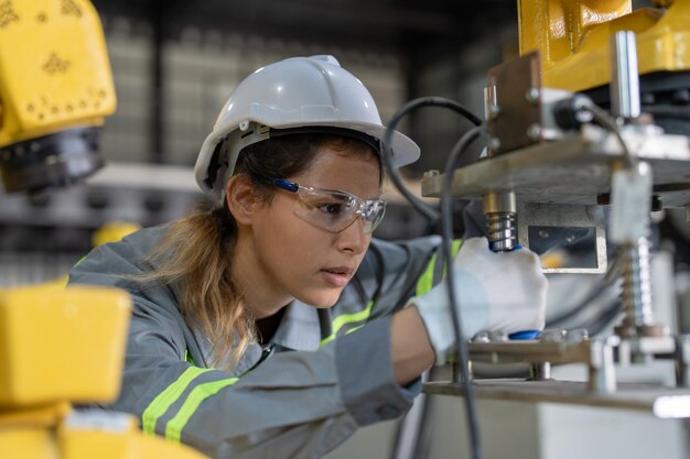 Foto vrouwelijke ingenieur die de machine van robotarmen in de fabriek controleert en onderhoudt