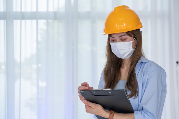Vrouwelijke ingenieur draagt een gezichtsmasker met gele veiligheidshelm controleer de juistheid van de constructie