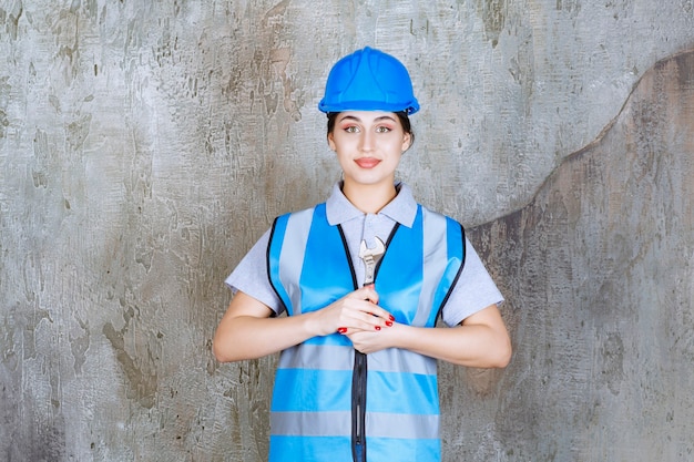 Vrouwelijke ingenieur in blauw uniform en helm met een metalen moersleutel.