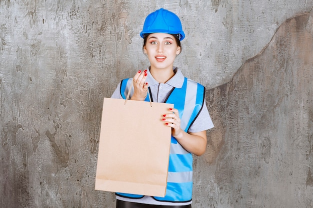 Vrouwelijke ingenieur in blauwe helm en uitrusting met een kartonnen boodschappentas.