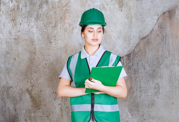 Vrouwelijke ingenieur in groen uniform en helm met de projectmap.