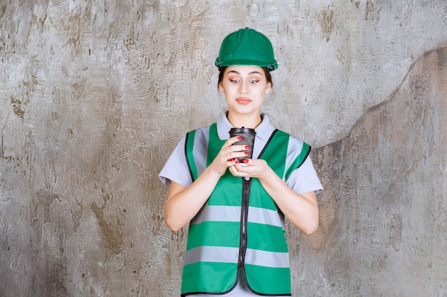 Vrouwelijke ingenieur in groen uniform en helm met een zwarte koffiekop