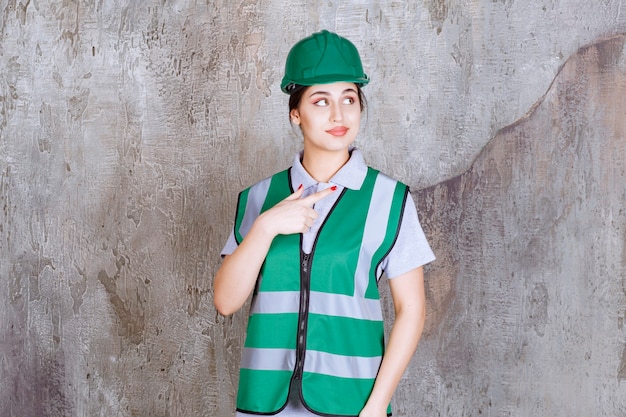 Vrouwelijke ingenieur in groen uniform en helm met rechterkant.