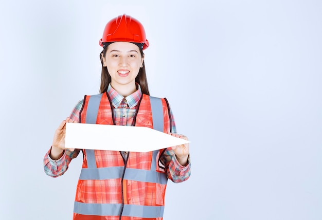 Vrouwelijke ingenieur in rode helm met een pijl die naar rechts wijst.