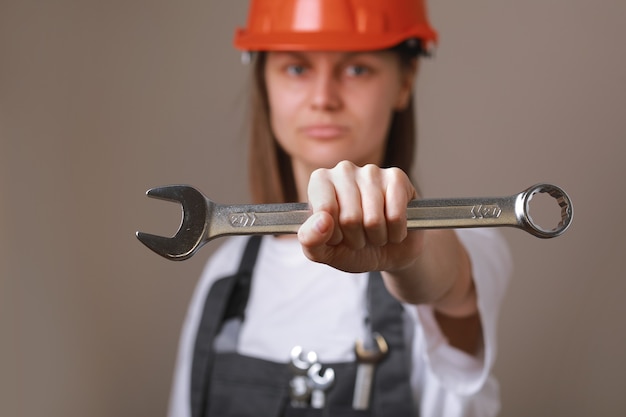 Vrouwelijke ingenieur werknemer in een uniform en veiligheidshelm met gereedschap, moersleutel in haar handen en tonen in de camera.