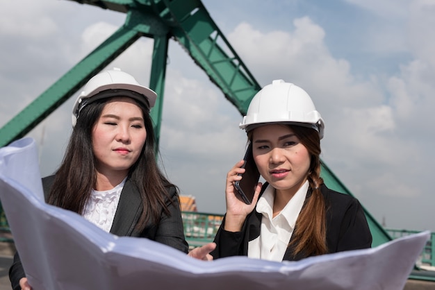 Vrouwelijke ingenieurs houden radio, blauwdrukken en rapporten, controleschema's voor werknemers in de energiesector.