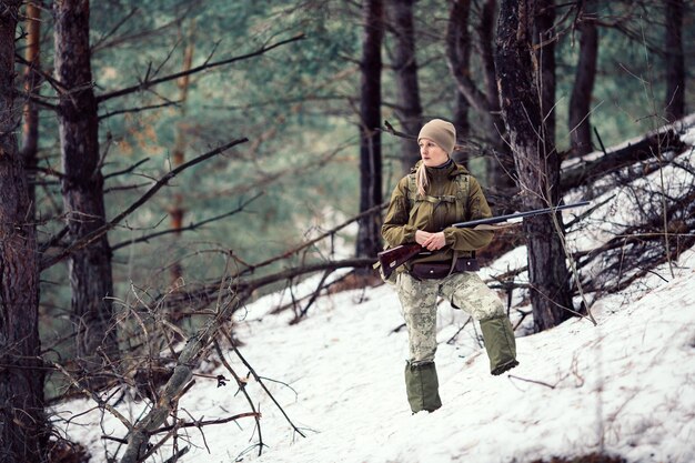 Vrouwelijke jager in camouflagekleding klaar om te jagen met pistool en wandelen in het bos
