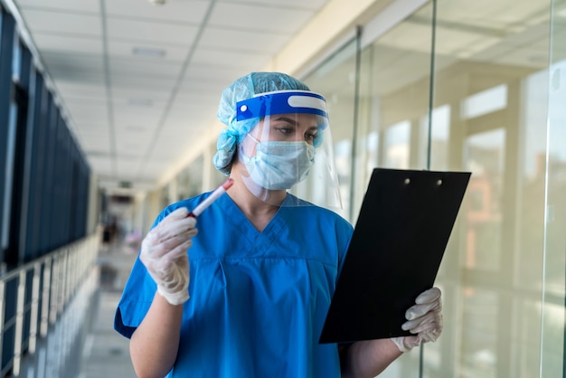 Vrouwelijke jonge arts in handschoenen die een buis met testbloed covid-19 in kliniek houden. positief testresultaat