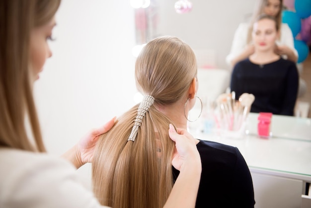 Vrouwelijke kapper maakt een kapsel voor een blond meisje in een schoonheidssalon