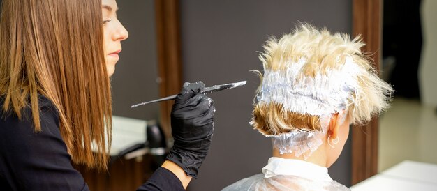 Vrouwelijke kapper verven kort blond haar van een jonge vrouw in een kapsalon