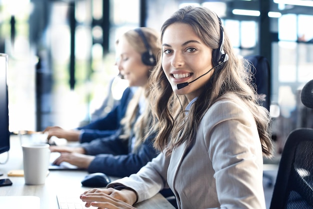 Vrouwelijke klantenservicemedewerker met headset en lachend met collega's op de achtergrond