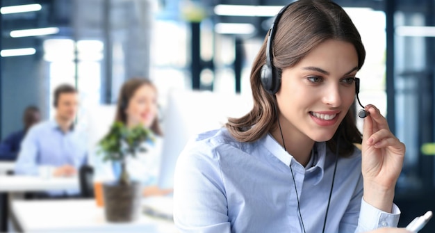 Vrouwelijke klantenservicemedewerker met headset en lachend met collega's op de achtergrond