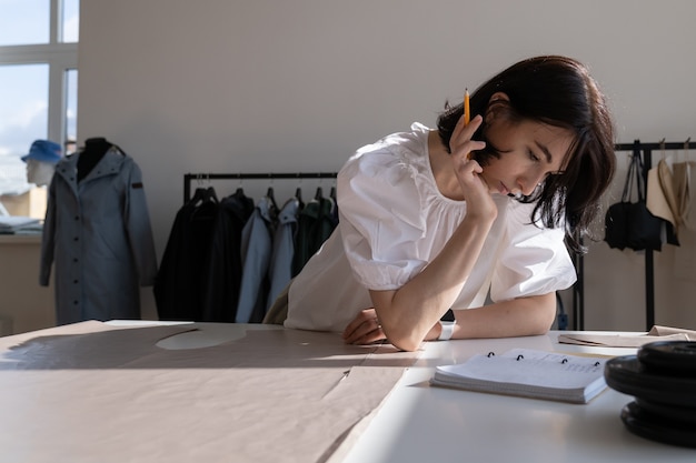 Vrouwelijke kledingontwerper in studio peinzend denk aan doekmaten voor toekomstige collectie op het werk