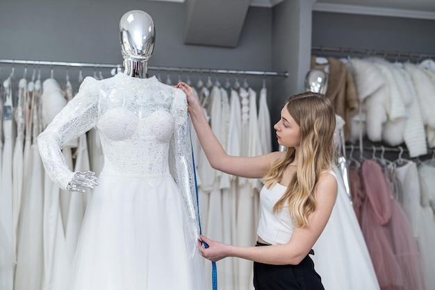 Vrouwelijke kleermaker gebruikt meetlint voor het meten van nieuwe trouwjurk op mannequin in de winkel