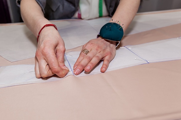 Vrouwelijke kleermakershanden met doek, patroon en naald in de werkplaats