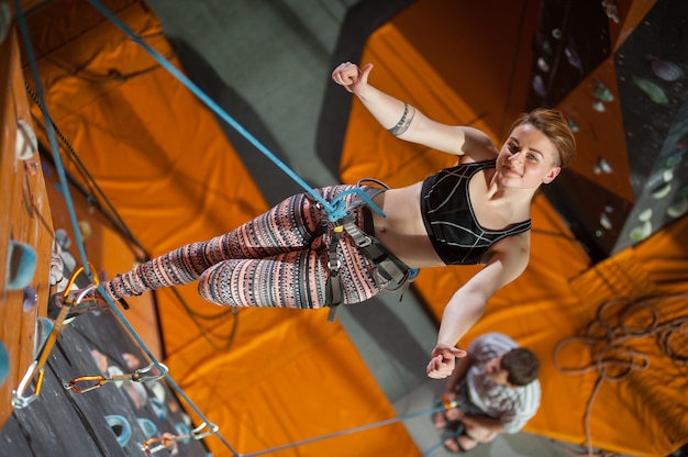 Vrouwelijke klimmer is klimmen op indoor rotsklimmende muur