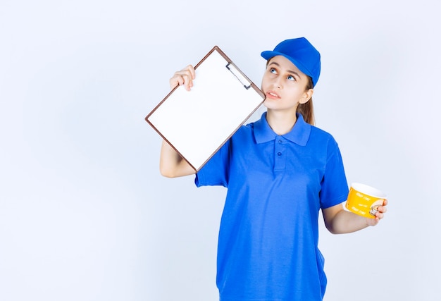 Vrouwelijke koerier in blauw uniform die een afhaalnoedelbeker vasthoudt en de handtekeninglijst aan de klant presenteert.