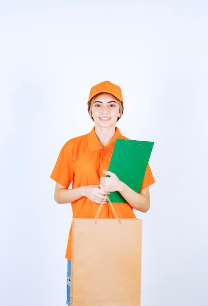 Vrouwelijke koerier in oranje uniform met een kartonnen boodschappentas en het controleren van de groene klantenlijst