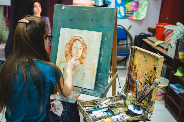 Vrouwelijke kunstenaar die op canvas op schildersezel in kunststudio schilderen