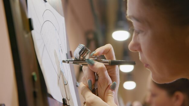 Vrouwelijke kunstenaar leert schilderen met airbrush met acrylverfpapier en schildersezel binnenshuis