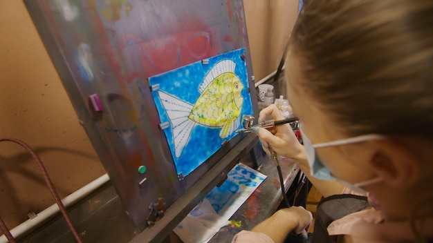 Vrouwelijke kunstenaar leert schilderen met airbrush met acrylverfpapier en schildersezel binnenshuis