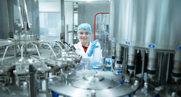 Vrouwelijke kwaliteitscontrolewerkster inspecteert een waterfles op de productielijn in een drinkwaterfabriek.